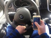 osoba trzymająca kierownicę pojazdu jedną ręką, a drugą ręką korzystająca z telefonu komórkowego