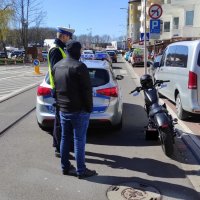 oznakowany radiowóz; umundurowany Policjant obok mężczyzna w kominiarce, niebieskich spodniach i czarnej kurtce; motocykl koloru czarnego