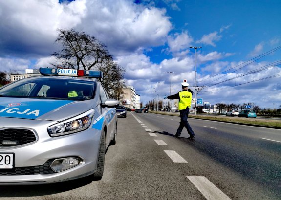 umundurowany policjant ruchu drogowego i radiowóz na drodze