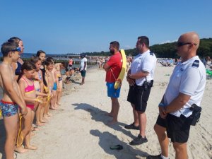 policjanci, ratownik wopr i grupa dzieci na plaży