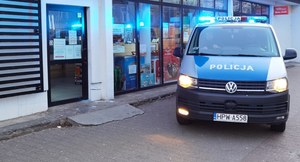 oznakowany radiowóz policji, policjant w cywilnych ciuchach przed sklepem spożywczym