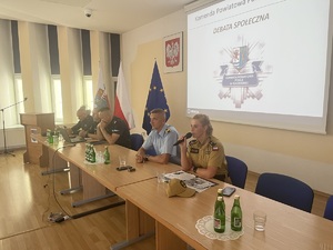 przy ławie umundurowani policjanci i funkcjonariusze a za nimi napis debata społeczna i logo KPP Kołobrzeg