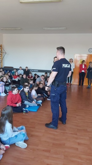 umundurowany policjant, grupa dzieci w szkolnej sali gimnastycznej