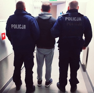 trzy osoby stojące tyłem- dwóch umundurowanych policjantów i mężczyzna