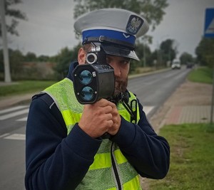 umundurowany policjant ruchu drogowego na drodze, trzymający miernik prędkości