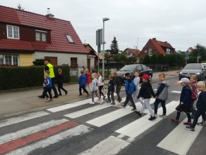 Umundurowany policjant wraz z grupką dzieci na przejściu dla pieszych