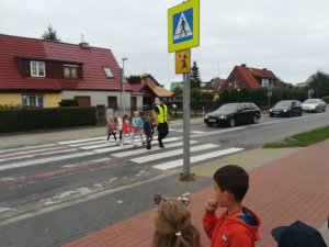 Umundurowany policjant wraz z grupką dzieci na przejściu dla pieszych
