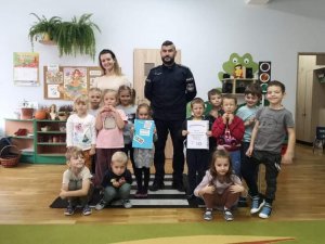 umundurowany funkcjonariusz policji, kobieta i gromadka dzieci w przedszkolu
