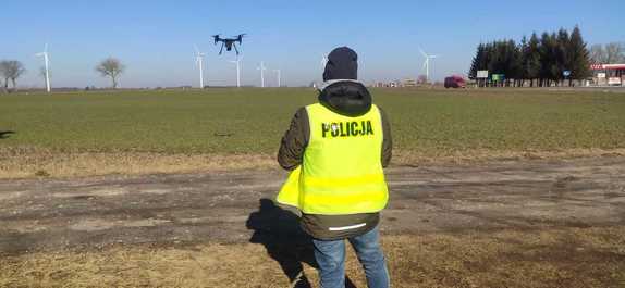 Policjant w kamizelce odblaskowej i dron na polu przy drodze
