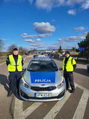 dwóch umundurowanych policjantów na drodze przy oznakowanym radiowozie