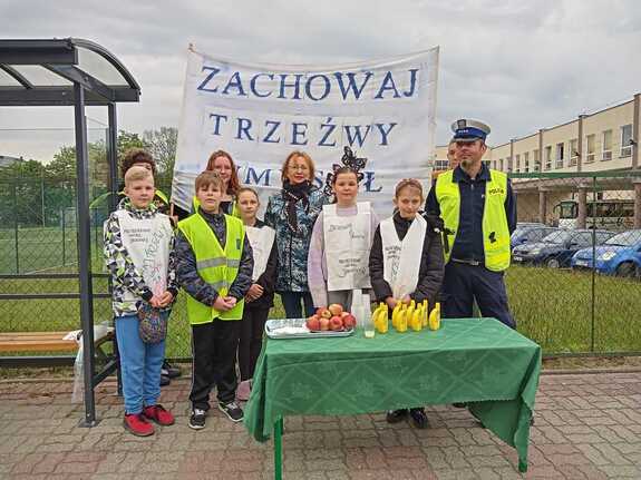 umundurowany funkcjonariusz policji z grupką dzieci na tle plakatu "zachowaj trzeźwy umysł"
