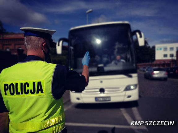 umundurowany policjant w odblaskowej kamizelce, w tle biały autobus