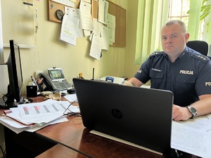 umundurowany policjant za biurkiem, laptop na biurku, zapisane kartki na biurku