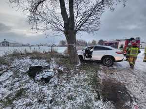 uszkodzony bok białego pojazdu osobowego na drodze pokrytej śniegiem, strażacy państwowej straży pożarnej, drzewo