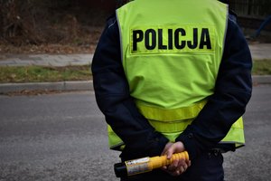 umundurowany policjant stojący tyłem na drodze, trzyma w rękach żółty alcoblow