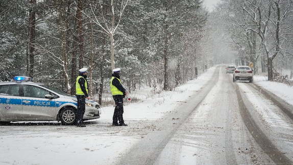 droga, śnieg na drodze, oznakowany radiowóz policyjny i dwóch umundurowanych policjantów