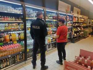 umundurowany policjant, ekspedientka, w tle półki sklepowe z alkoholem