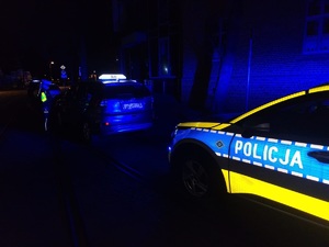 oznakowany radiowóz i pojazd osobowy w nocy na drodze, umundurowany policjant