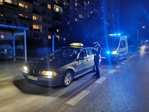 oznakowany radiowóz i pojazd osobowy w nocy na drodze, umundurowany policjant