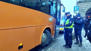 Stojący na drodze umundurowany policjant, mężczyzna z kamerą, autobus koloru pomarańczowego