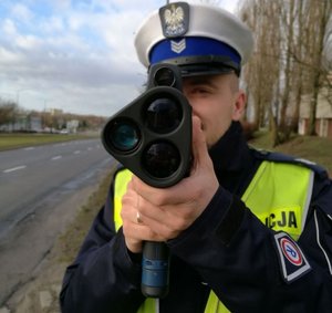 policjant umundurowany trzymający ręczny miernik prędkości na drodze