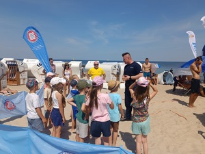 plaża, umundurowani funkcjonariusze, grupa dzieci i dorosłych