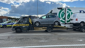 Laweta załadowanymi dwoma pojazdami, w tle oznakowany radiowóz policyjny