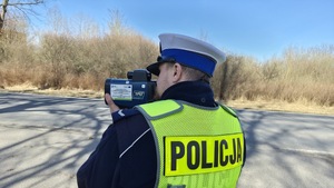 policjant umundurowany w białej czapce mierzy prędkość ręcznym miernikiem prędkości